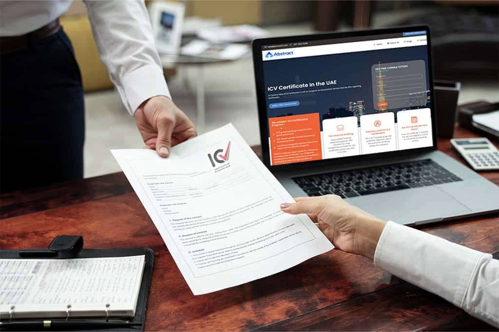Two people exchange an ICV (In-Country Value) certificate across a wooden desk. A laptop is open on the desk, displaying a website detailing the process of obtaining ICV certification in the UAE. An open binder and a calculator are also on the desk.