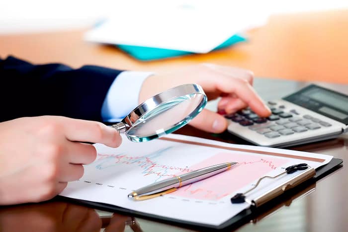 A person is holding a pen, potentially preparing to write or take notes. The setting appears to be an indoor office environment, surrounded by various office supplies and equipment. This includes a computer and additional stationery items that suggest an atmosphere focused on productivity and organization. The person is in an ICV Consulting Service Office in Dubai, emphasizing the professional and organized nature of the environment.