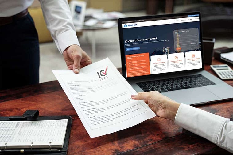 Two people exchange an ICV (In-Country Value) certificate across a wooden desk. A laptop is open on the desk, displaying a website detailing the process of obtaining ICV certification in the UAE. An open binder and a calculator are also on the desk.
