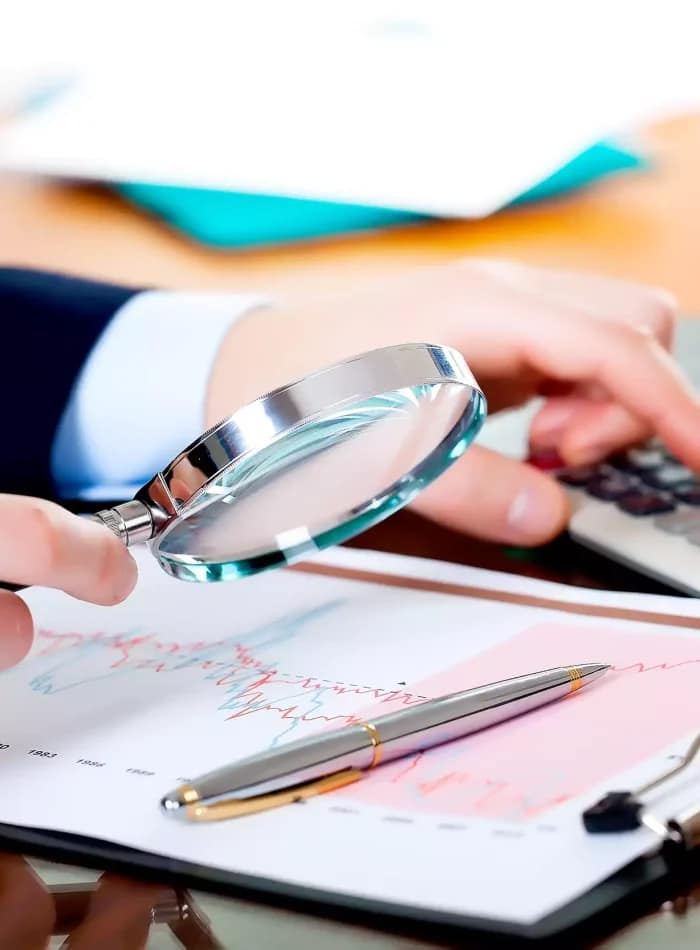 A person is holding a pen, potentially preparing to write or take notes. The setting appears to be an indoor office environment, surrounded by various office supplies and equipment. This includes a computer and additional stationery items that suggest an atmosphere focused on productivity and organization. The person is in an ICV Consulting Service Office in Dubai, emphasizing the professional and organized nature of the environment.